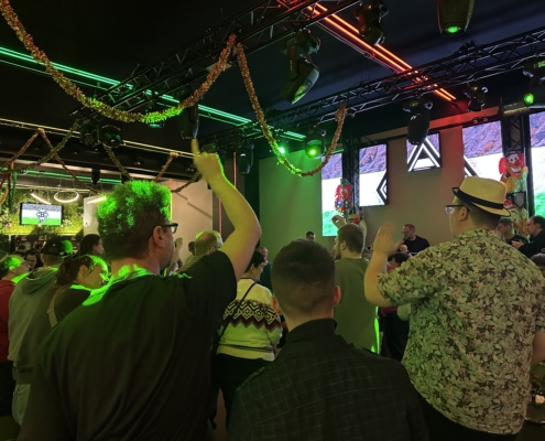 Menschen feiern in einem lebhaften Nachtclub mit bunten Lichtern und Dekorationen. Die Stimmung ist festlich, während die Gäste ihre Hände in die Luft heben und die Musik genießen.