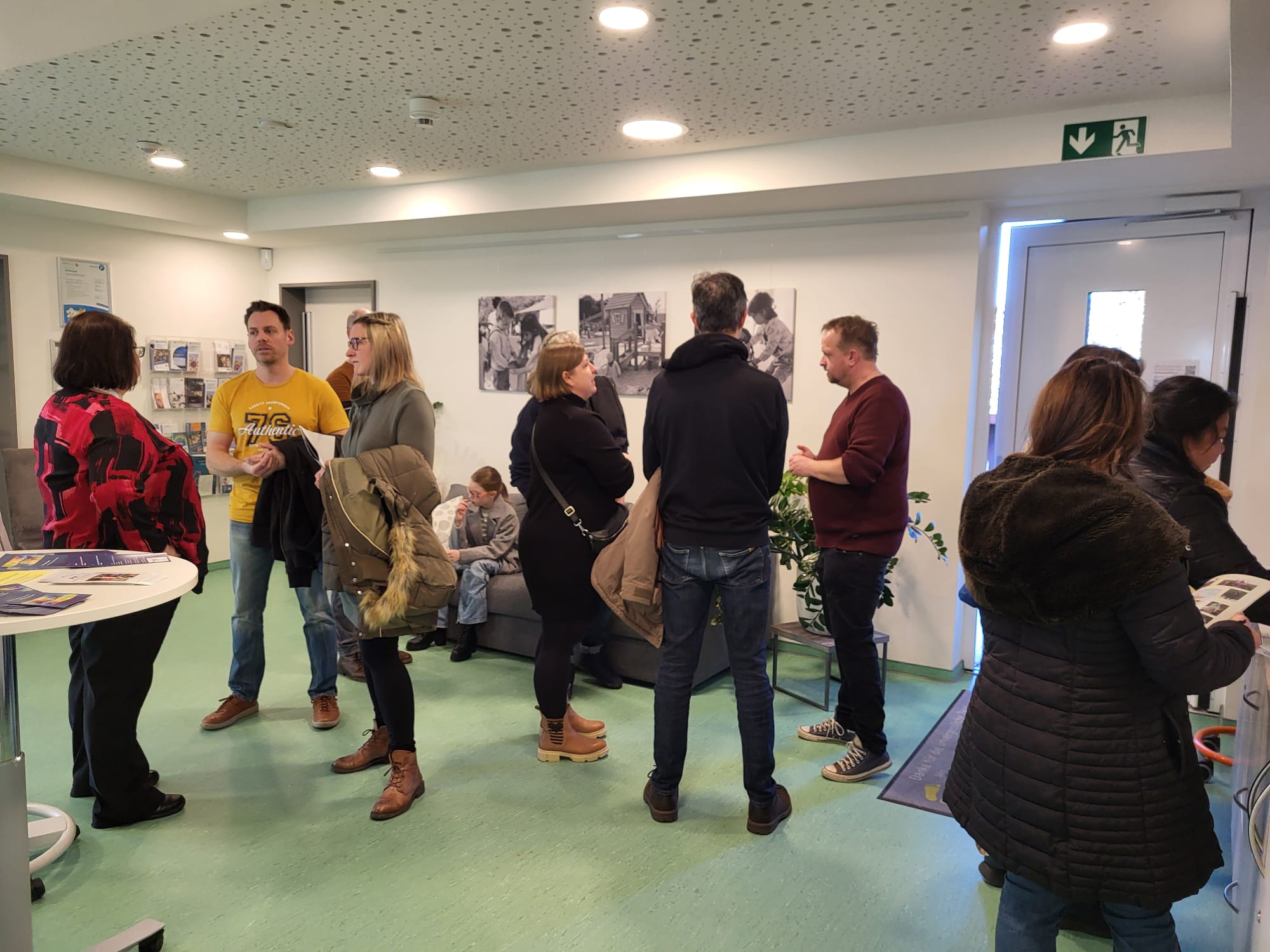 Menschen stehen in einem Raum mit grünen Wänden. Sie unterhalten sich.