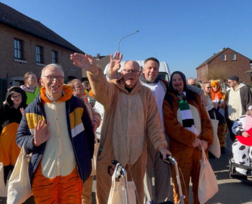 Menschen in bunten Kostümen feiern in einer fröhlichen Parade unter blauem Himmel. Einige Teilnehmer tragen Tierkostüme, während andere bunte Accessoires und Masken präsentieren. Die Atmosphäre ist festlich und lebhaft.