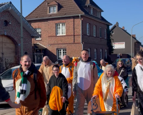 Menschen in Tierkostümen beim Umzug in einer Stadt, umgeben von Wohnhäusern, bei sonnigem Wetter.