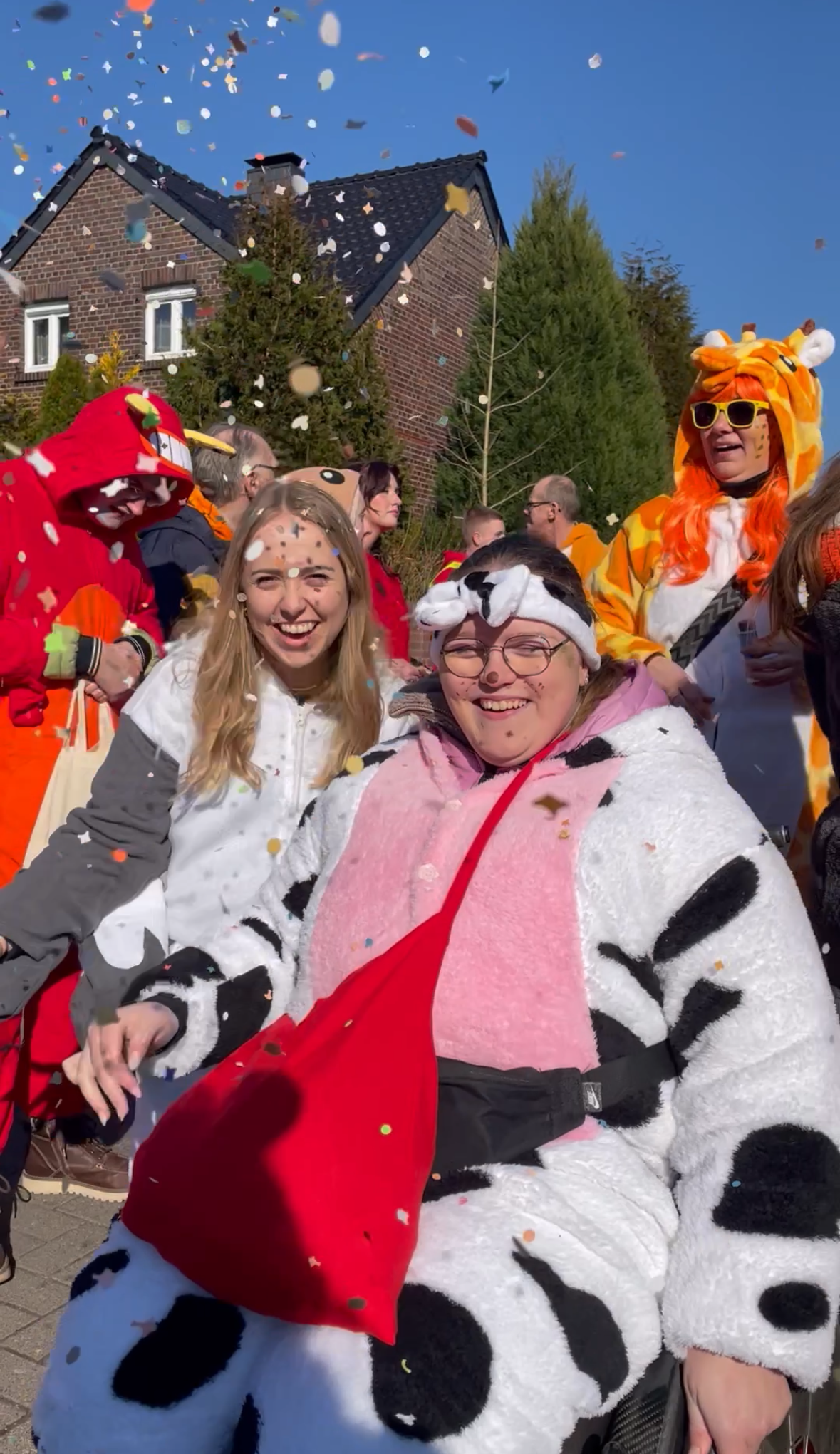 Zwei Frauen in Kuhkostüme stehen lachend vor einem Haus. Es schneit Konfetti.