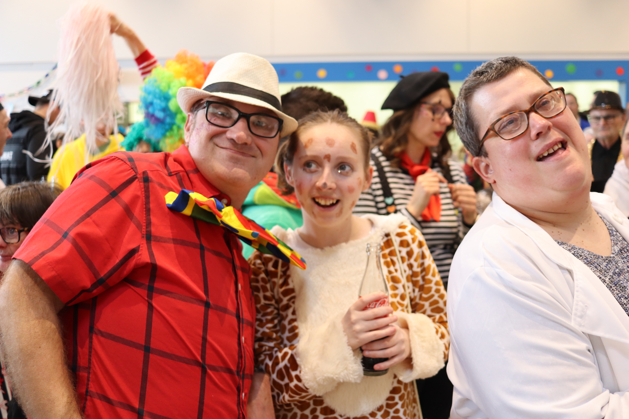 Drei Personen in bunten Kostümen feiern fröhlich auf einer Veranstaltung, umgeben von festlicher Dekoration.