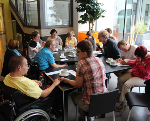 Menschen sitzen an einem Tisch. Einige trinken Kaffee. Sie unterhalten sich.