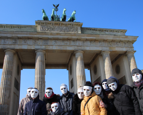 Menschen mit Masken stehen vor dem Brandenburger Tor.
