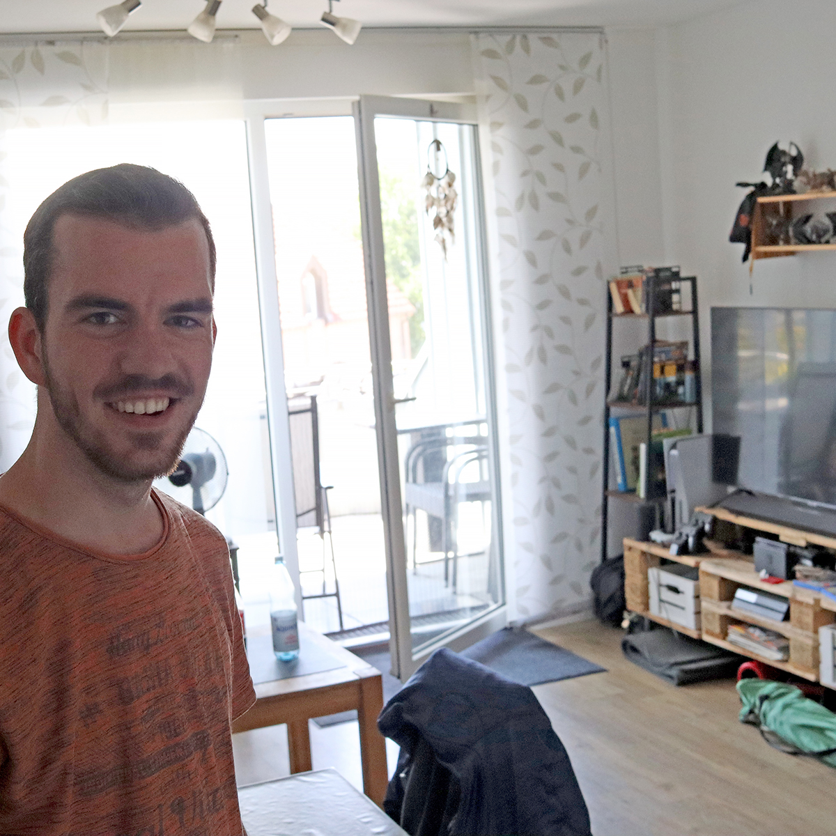 Junger Mann steht im Wohnzimmer und lächelt in die Kamera