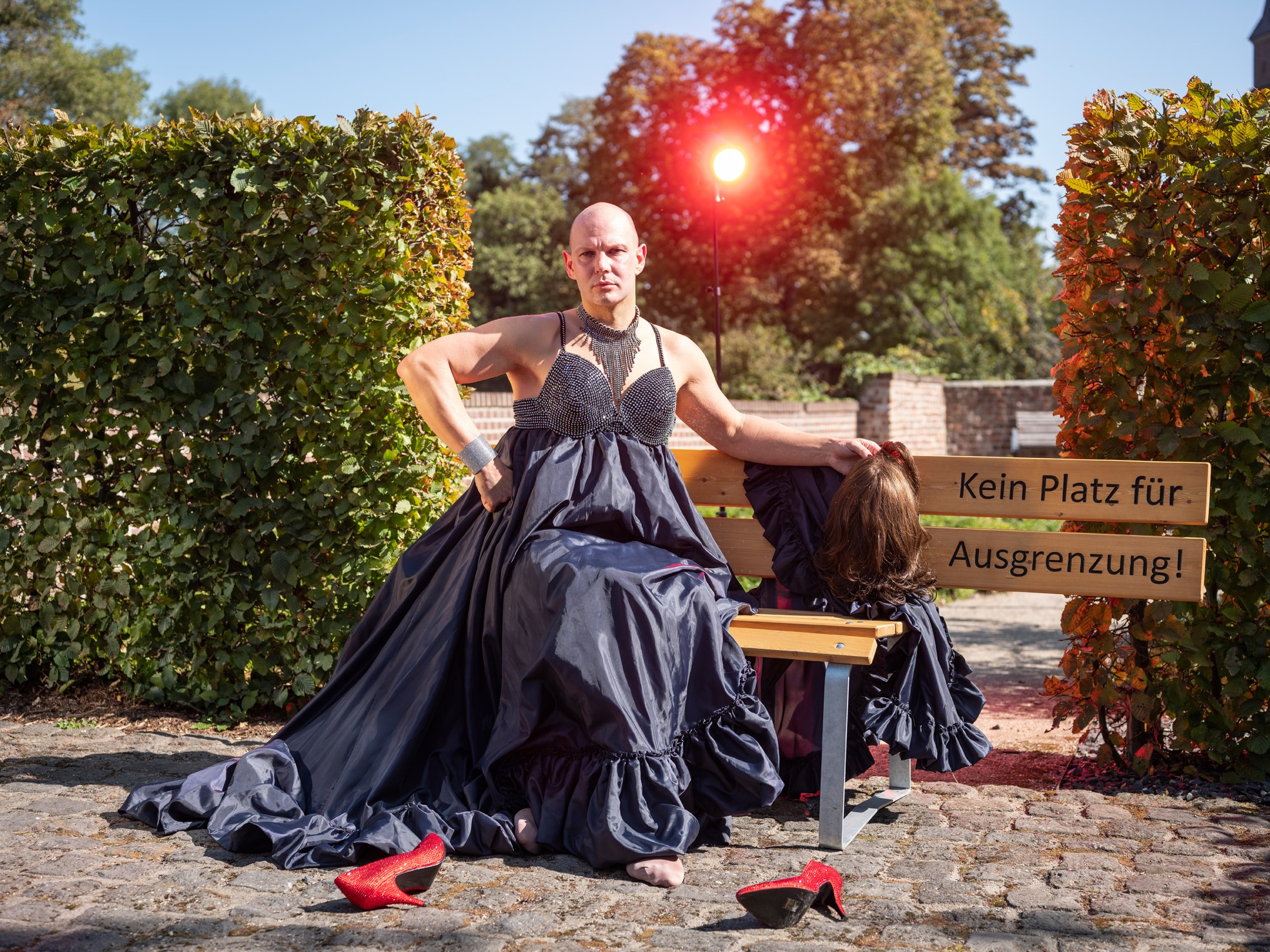 Eine Frau mit einem langen Kleid sitzt auf einer Bank im Freien. Sie trägt rote Schuhe.