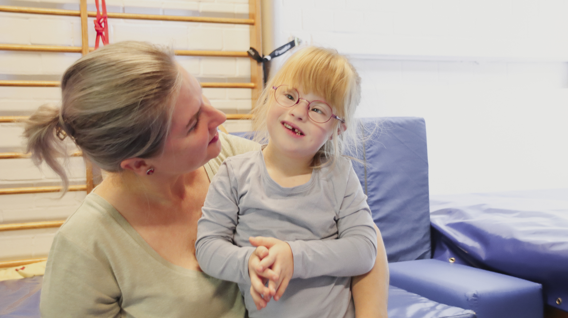 Eine Frau lächelt ein Kind an, das Kind lacht und steht im Arm der Frau.