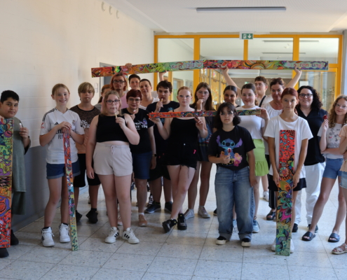 Gruppe von Schülern in einem Schulflur, die gemeinsam für ein Foto posieren, einige halten Bastelarbeiten in den Händen.