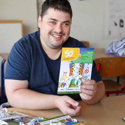 Ein Mann lächelt in die Kamera und hält stolz eine Karte hoch.