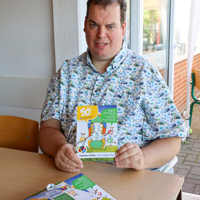 Ein Mann lächelt in die Kamera und hält stolz eine Karte hoch.