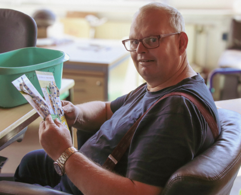 Ein Mann hält zwei Flyer in der Hand und lächelt in die Kamera.