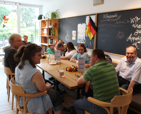 Menschen sitzen an einem Tisch in einem hellen Raum. Sie unterhalten sich und trinken etwas.