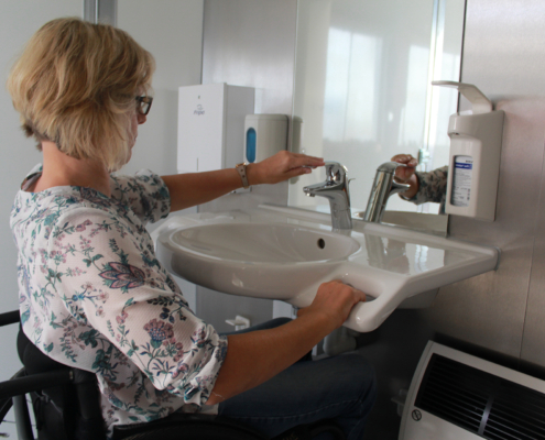 Toilette für Alle (2) Eine Frau wäscht sich am Waschbecken.