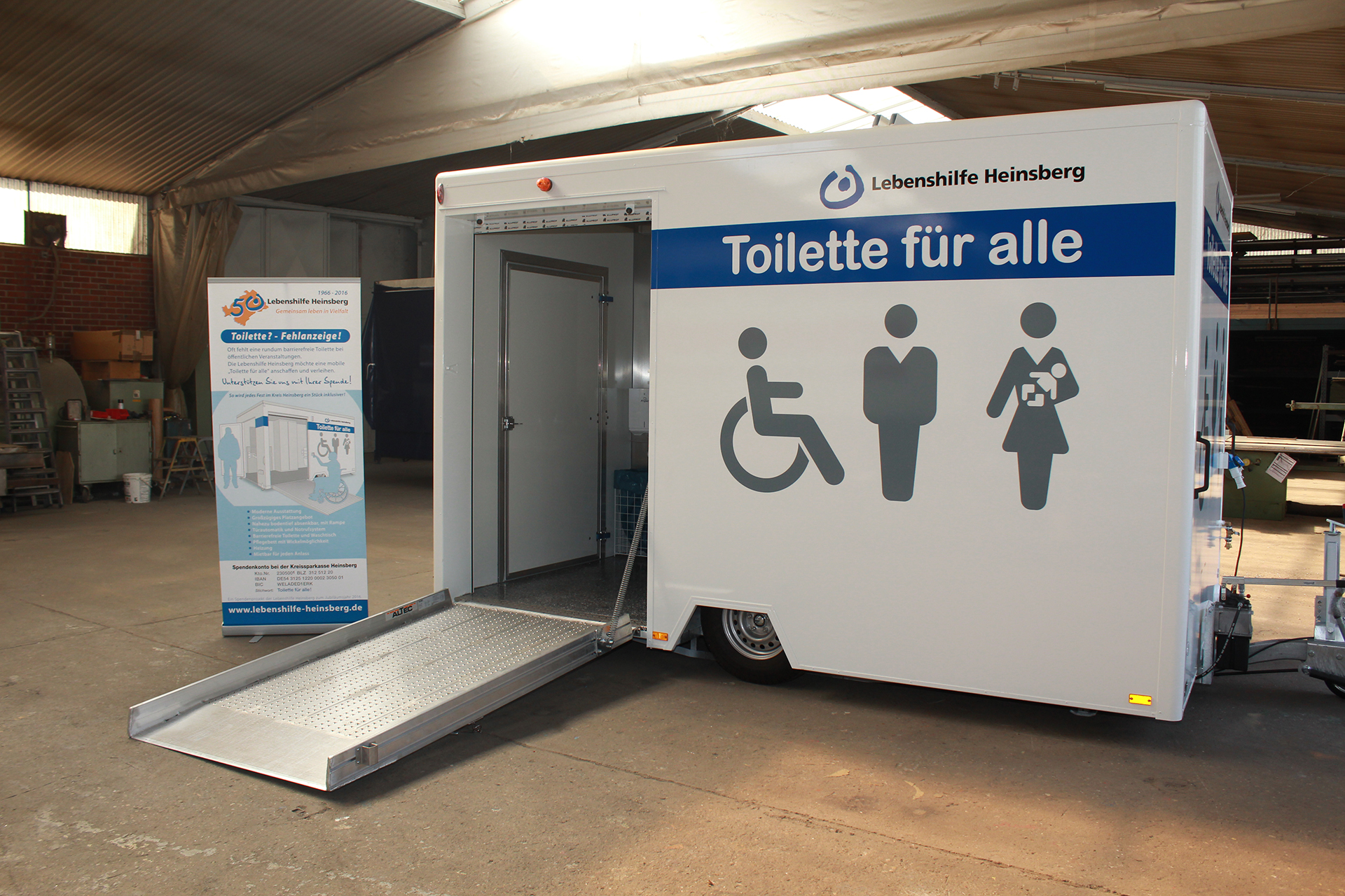 Toilette für Alle (24) Eine mobile Toilette mit einer Rampe. Sie ist weiß und steht auf einem Hof.