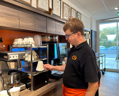 Ein Mann in einer Küche macht Kaffee. Er hat eine Kaffeemaschine bedient und hält eine Tasse.