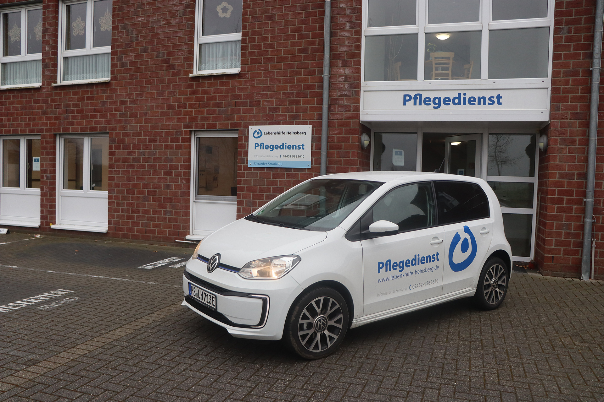 Ein weißes Auto steht vor einem roten Haus. Es ist ein schönes Wetter.