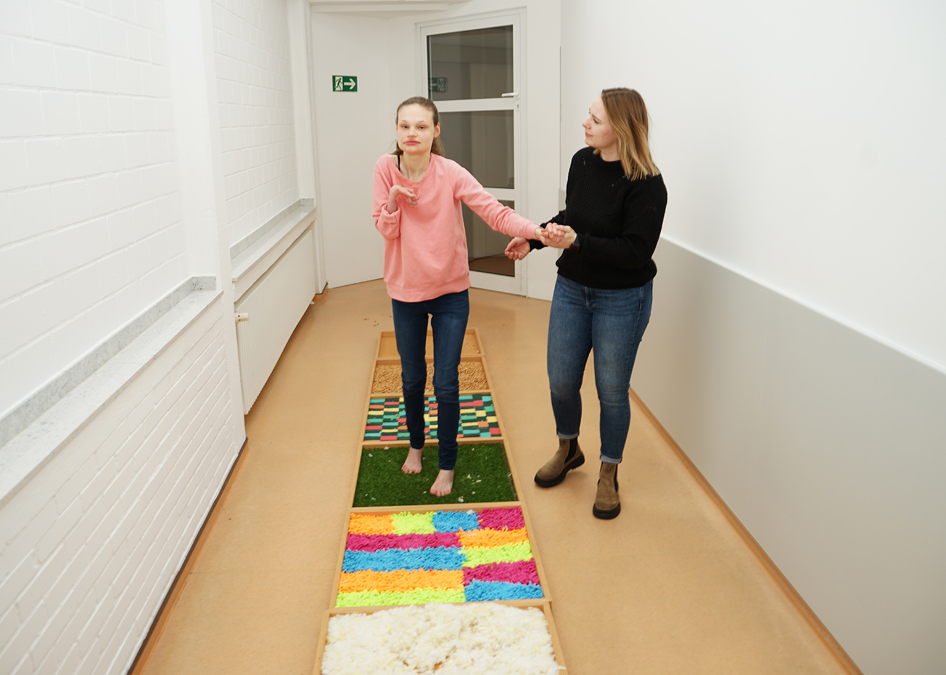 2023_Foerderbereich-2 Zwei Mädchen gehen auf einem Teppich. Eines trägt ein rotes Shirt, das andere ein schwarzes.