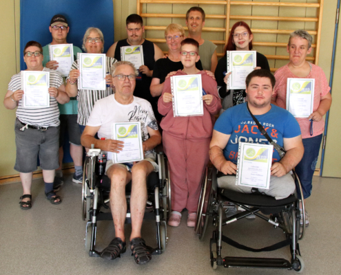 Ein Mann sitzt im Rollstuhl. Er hat ein rotes T-Shirt an. Er lächelt.