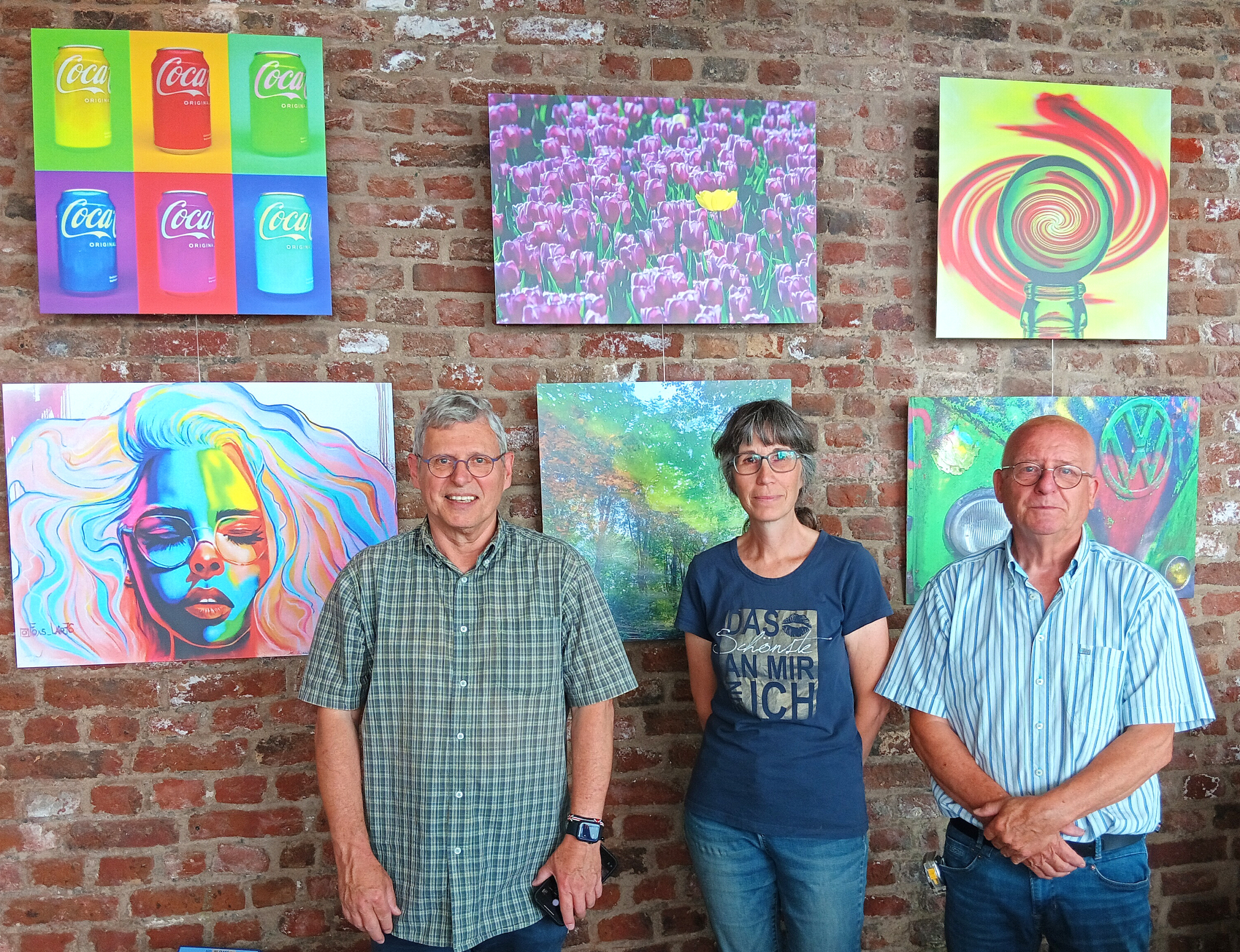 Zwei Personen stehen vor einem Bild. Das Bild zeigt ein Gesicht. Die Personen tragen Jeans und T-Shirts.