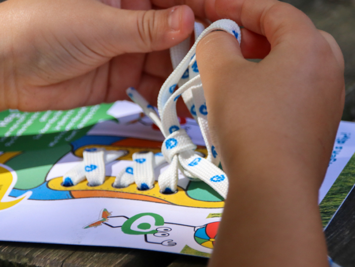 Eine Hand hält ein weißes Seil. Im Hintergrund sind grüne Bäume zu sehen.