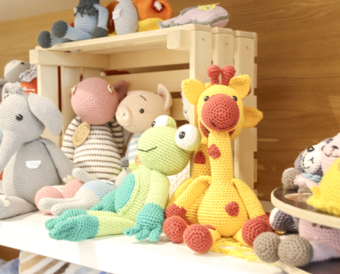 Süße Stofftiere liegen auf einem Holzregal. Es sind ein Elefant, ein Krokodil und ein Giraffe.