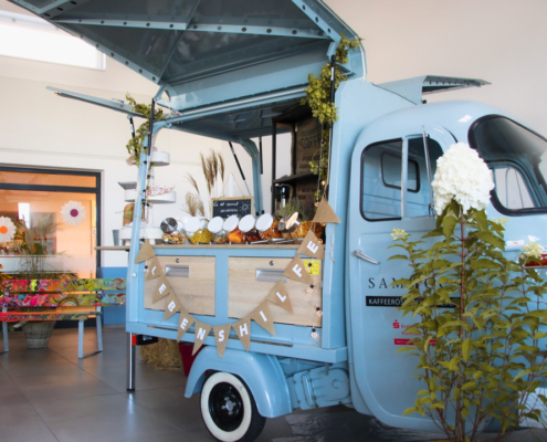 Ein blauer Lastwagen steht auf einem Hof. Er ist voll mit Blumen und Dingen zum Dekorieren.
