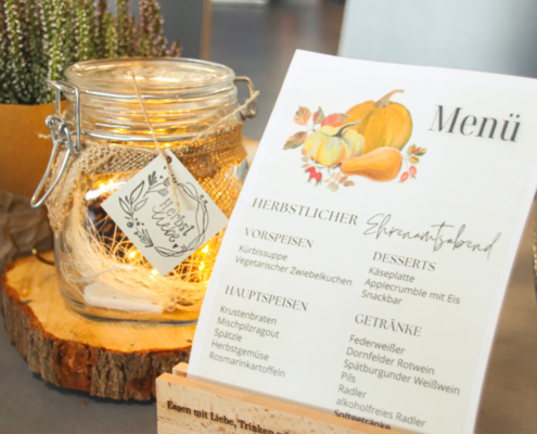 Ein herbstlich dekorierter Tisch mit Essen und Getränken. Es sind Teller, Gläser und eine Speisekarte zu sehen.