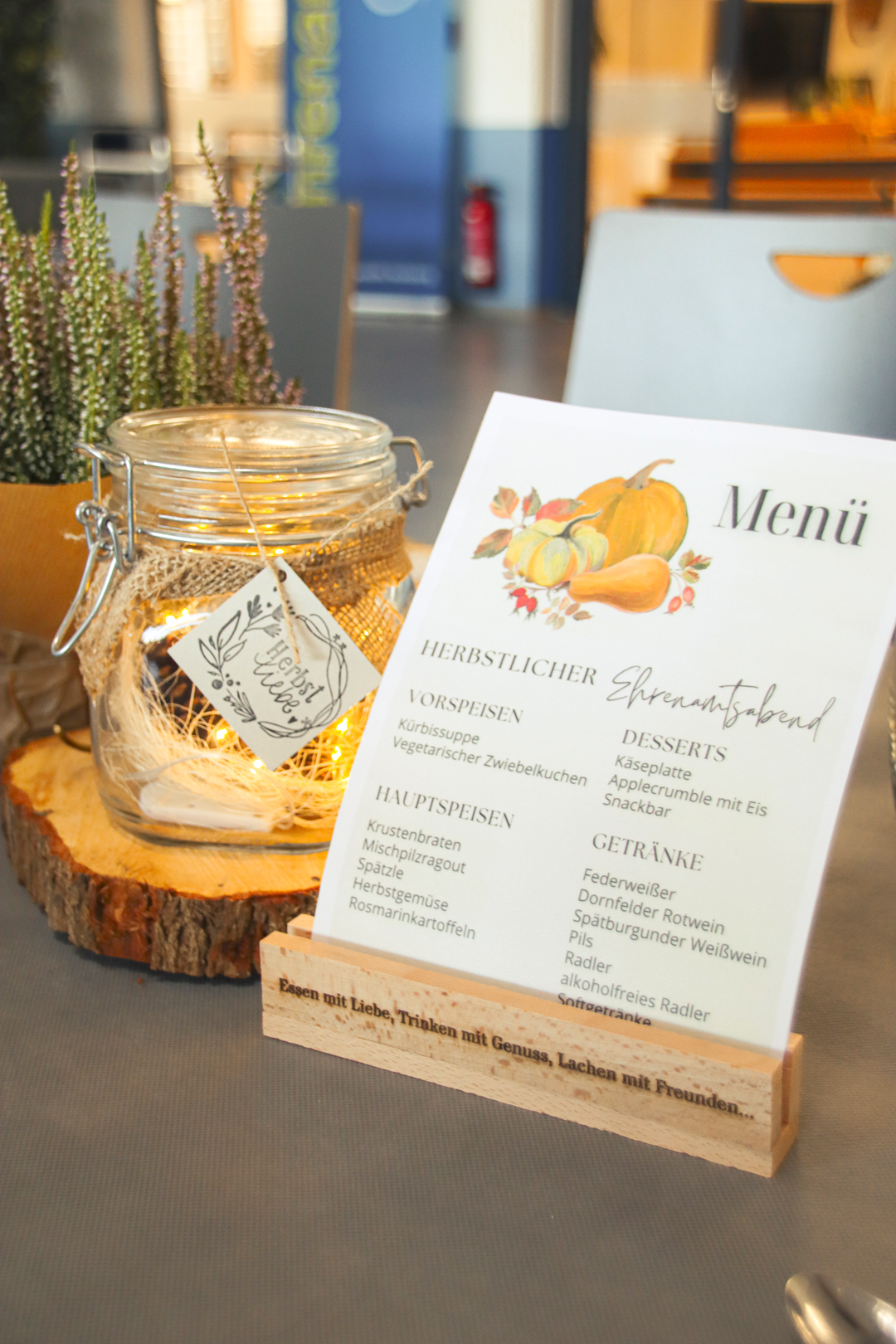Ein herbstlich dekorierter Tisch mit Essen und Getränken. Es sind Teller, Gläser und eine Speisekarte zu sehen.