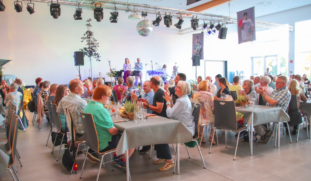 Viele Leute sitzen an Tischen. Es gibt Musik und Essen.