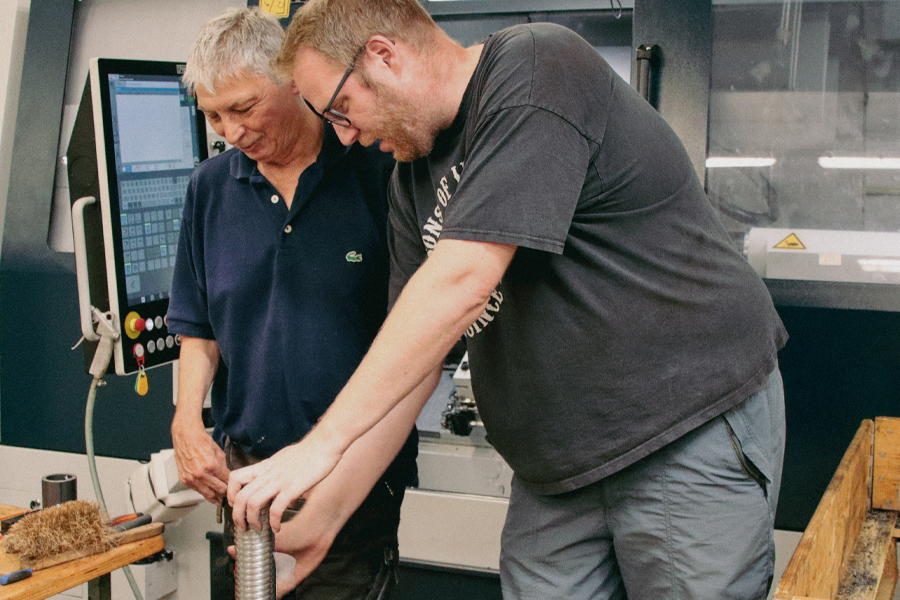 Ein Mann in blauer Jacke arbeitet an einer Maschine. Er hält etwas in der Hand.