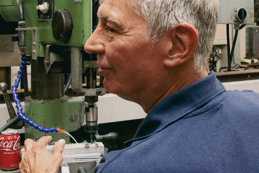 Ein Mann arbeitet mit einer Maschine. Er trägt ein blaues Hemd. Die Maschine ist grün.