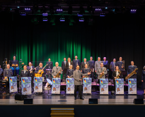 Eine große Gruppe von Musikern steht auf einer Bühne. Sie spielen verschiedene Instrumente.