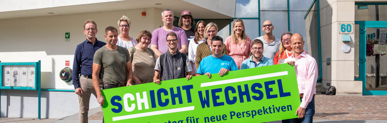 Eine Gruppe von Leuten steht vor einem Gebäude. Sie lächeln und schauen in die Kamera.