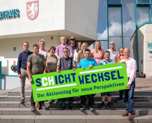 Eine Gruppe von Leuten steht vor einem Gebäude. Sie lächeln und schauen in die Kamera.