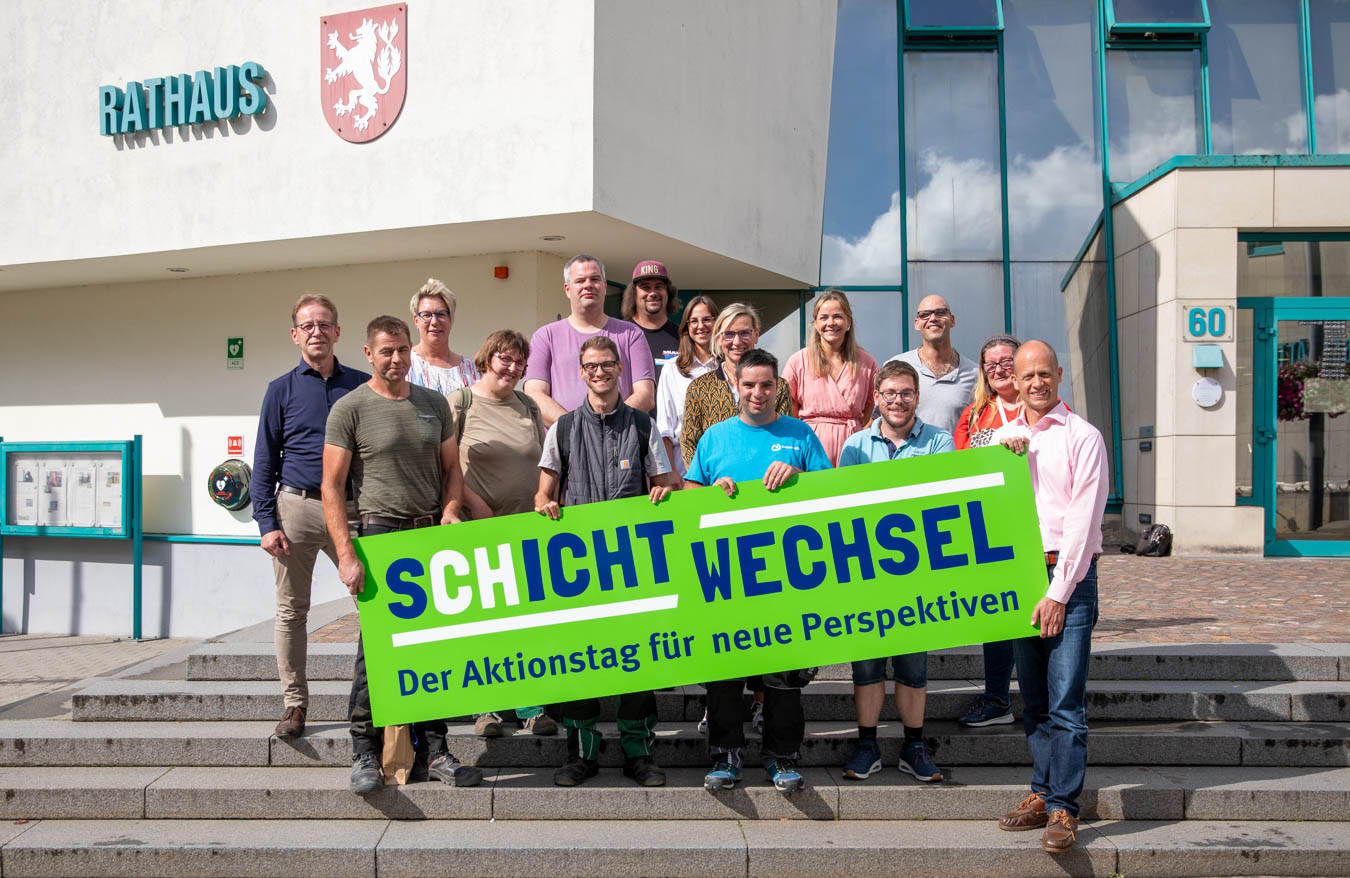 Eine Gruppe von Leuten steht vor einem Gebäude. Sie lächeln und schauen in die Kamera.