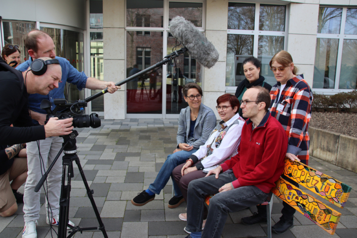 Eine Filmcrew filmt Menschen, die auf einer Bank sitzen.