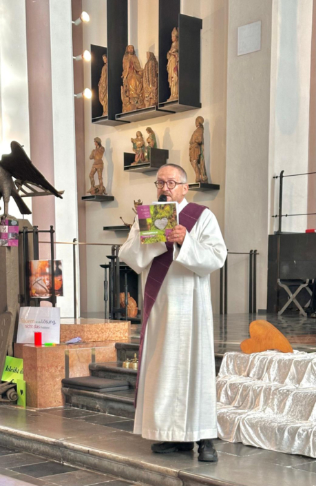 Ein Mann in weißer Kleidung steht vor einem Altar. Er hält ein Buch in der Hand.