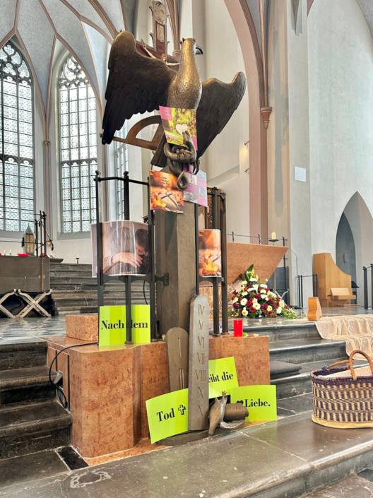 Eine große Statue steht in einer Kirche. Es gibt Blumen und Kerzen. Die Kirche ist hell und groß.