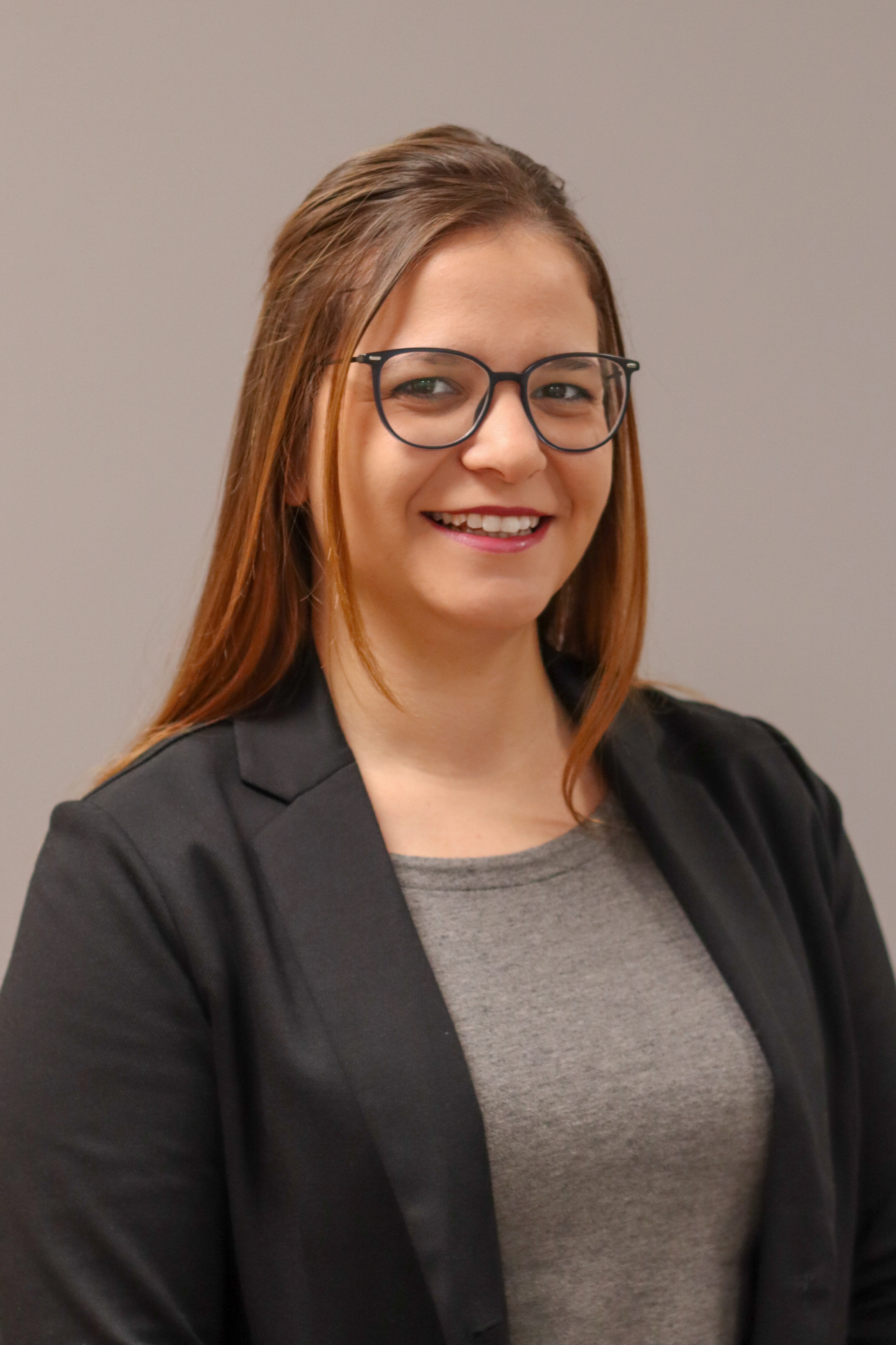 Katharina_Esser_2025 Eine Frau mit Brille lächelt in die Kamera. Sie trägt eine Jacke und ein graues T-Shirt.
