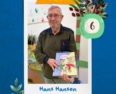 Ein älterer Mann steht im Garten. Er hat eine Brille und ein graues Shirt an. Er hält ein Buch in der Hand.