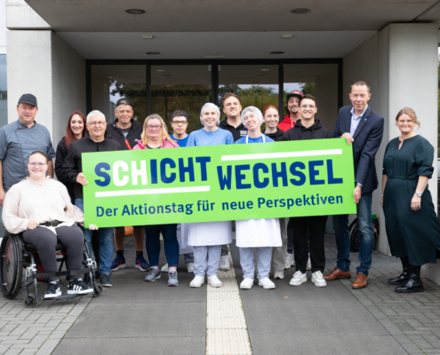 Eine Gruppe von Menschen steht vor einem Gebäude. Sie lächeln in die Kamera.