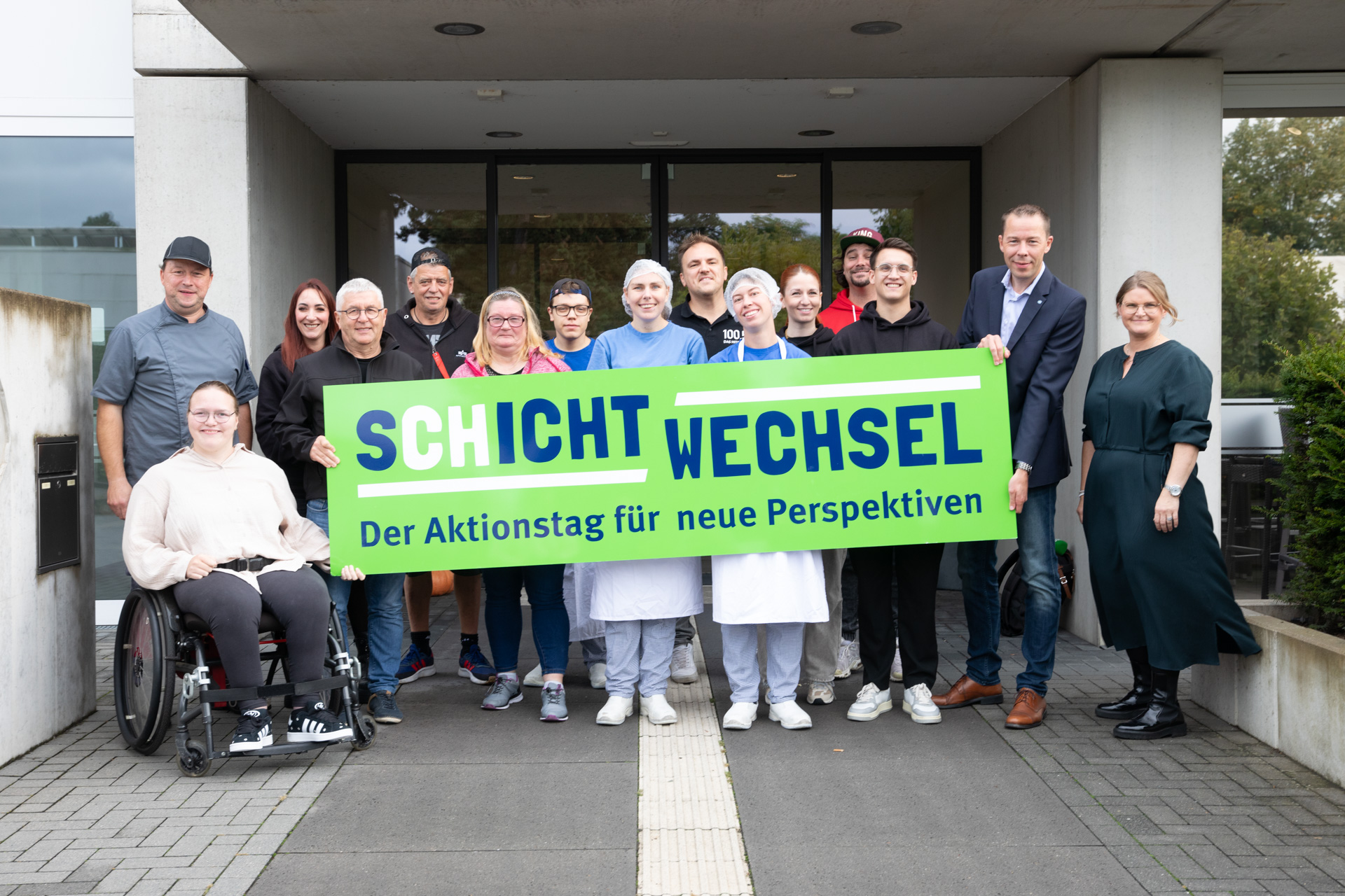 Eine Gruppe von Menschen steht vor einem Gebäude. Sie lächeln in die Kamera.