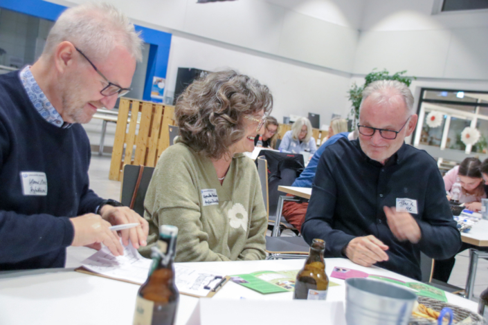 Drei Personen sitzen an einem Tisch. Sie schauen sich Unterlagen an.