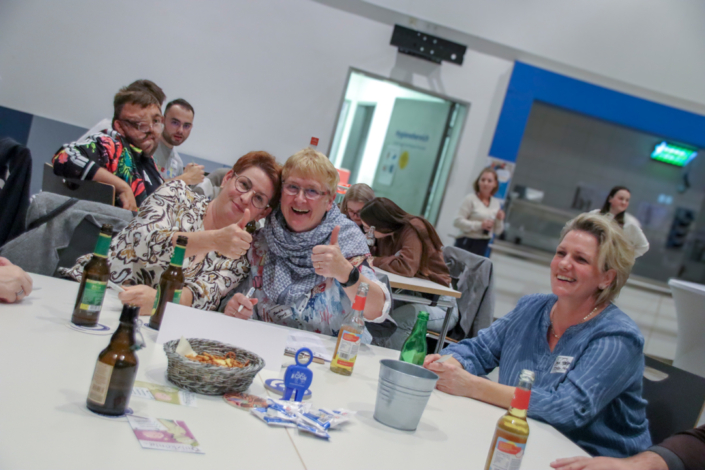 Eine Gruppe von Leuten sitzt an einem Tisch. Es gibt Bier und Essen. Alle lachen und sehen glücklich aus.