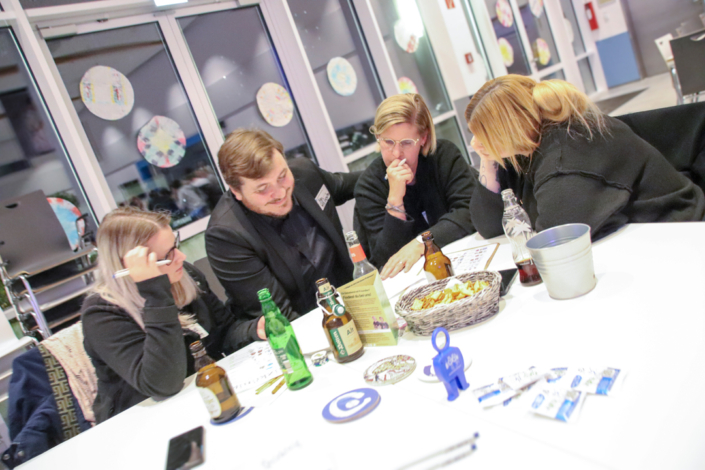 Leute sitzen an einem Tisch. Es gibt Bierflaschen und Essen auf dem Tisch.