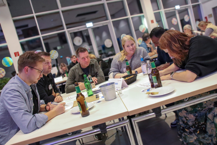 Eine Gruppe von Leuten sitzt an einem Tisch und unterhält sich. Es stehen Bierflaschen und Gläser auf dem Tisch.