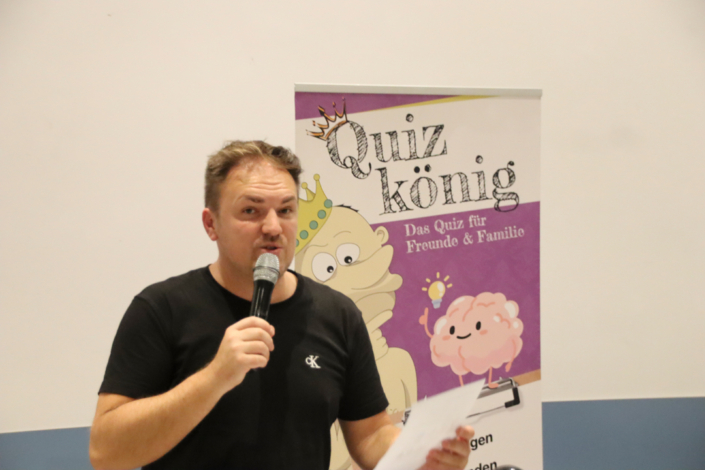 Ein Mann hält ein Mikrofon. Er spricht zu Leuten.