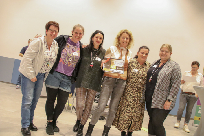 Vier Frauen stehen zusammen. Sie lächeln und schauen in die Kamera.