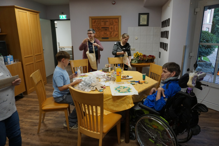 Menschen sitzen an einem Tisch. Sie basteln etwas mit Papier und Kleber.