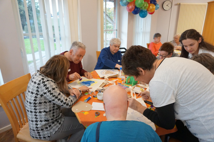 Menschen sitzen an einem Tisch. Sie malen und basteln mit Papier und Farben.